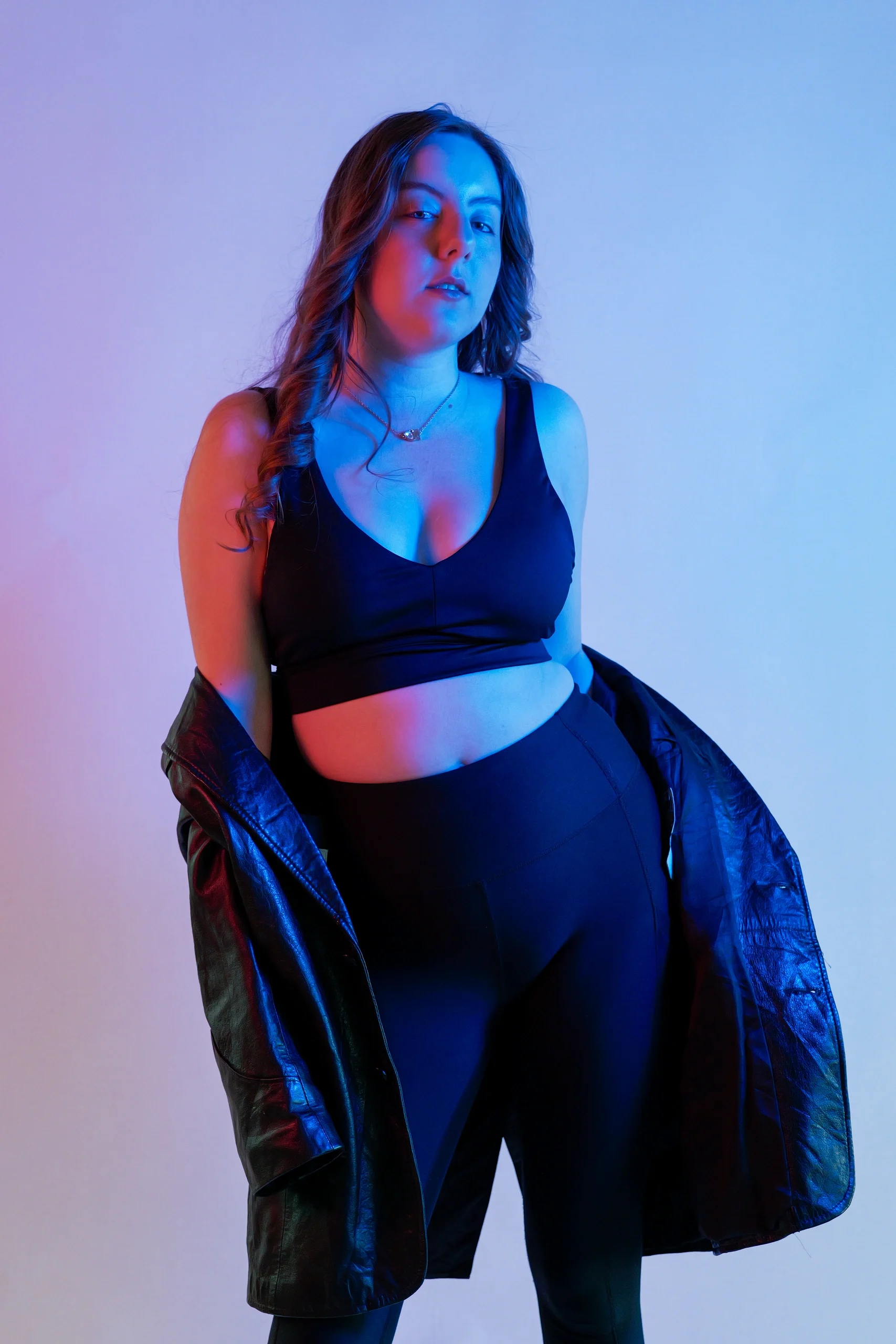 Studio portrait with split color gel lighting, black crop top and pants, draped leather jacket