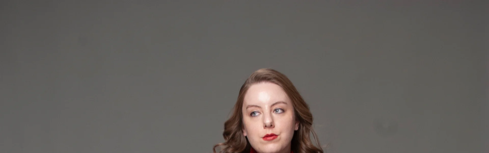 Full-length studio portrait in red velvet zip-up jacket and black gathered-skirt gown on gray backdrop