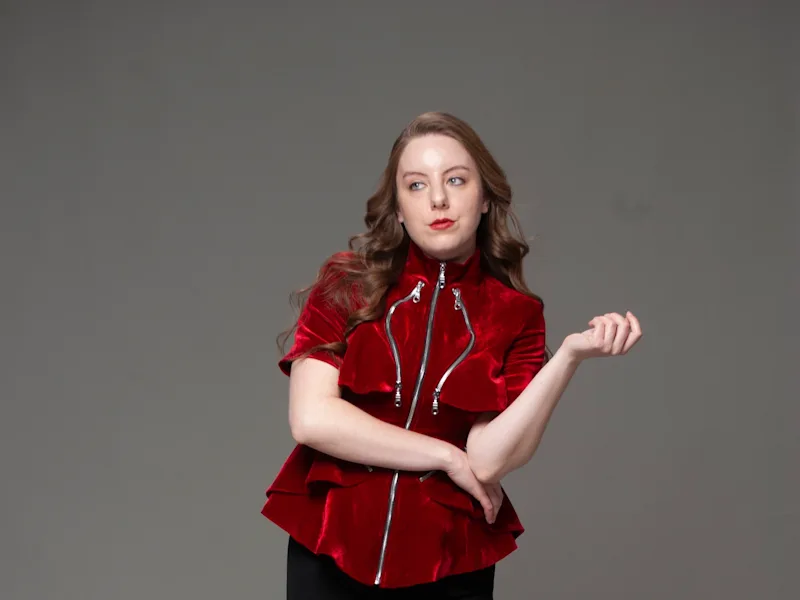 Full-length studio portrait in red velvet zip-up jacket and black gathered-skirt gown on gray backdrop