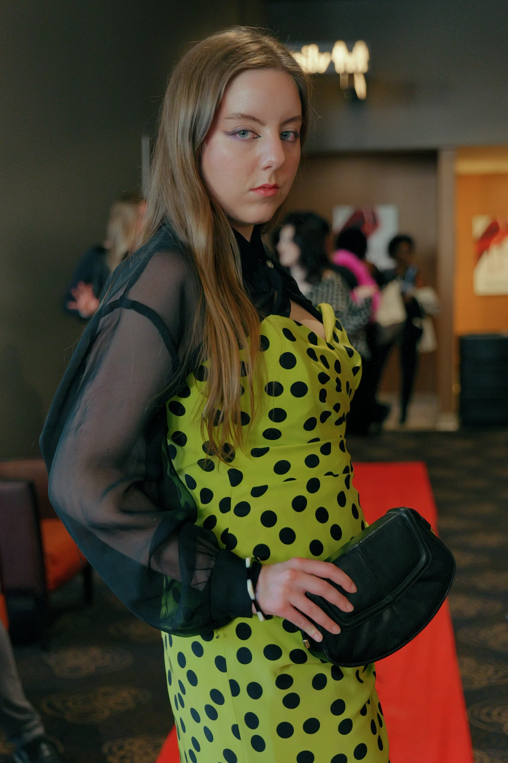 Model in yellow polka dot dress with sheer black sleeves and black clutch backstage at fashion show