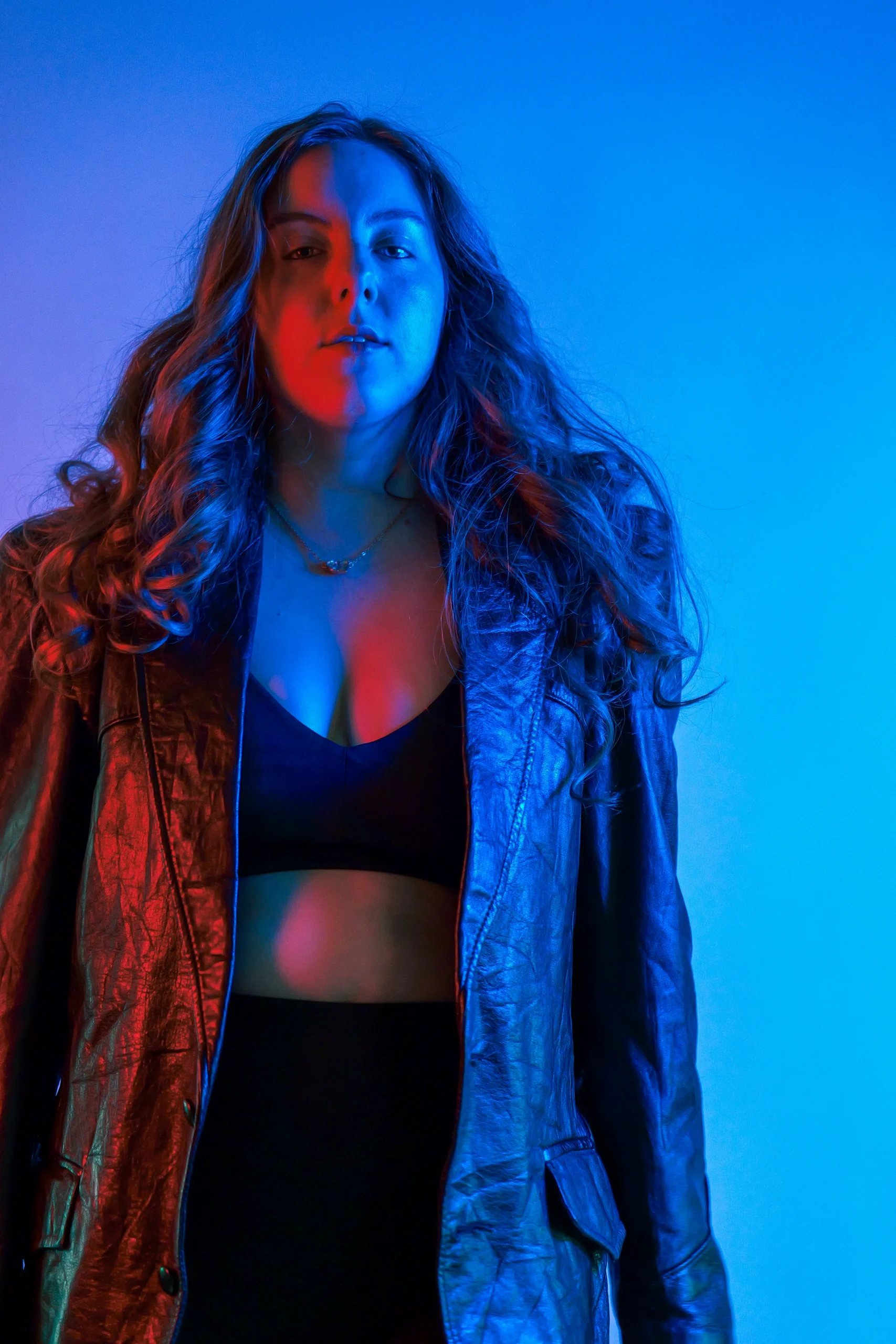 Studio full-body portrait with red-blue split lighting, denim jacket, black crop top, blue backdrop
