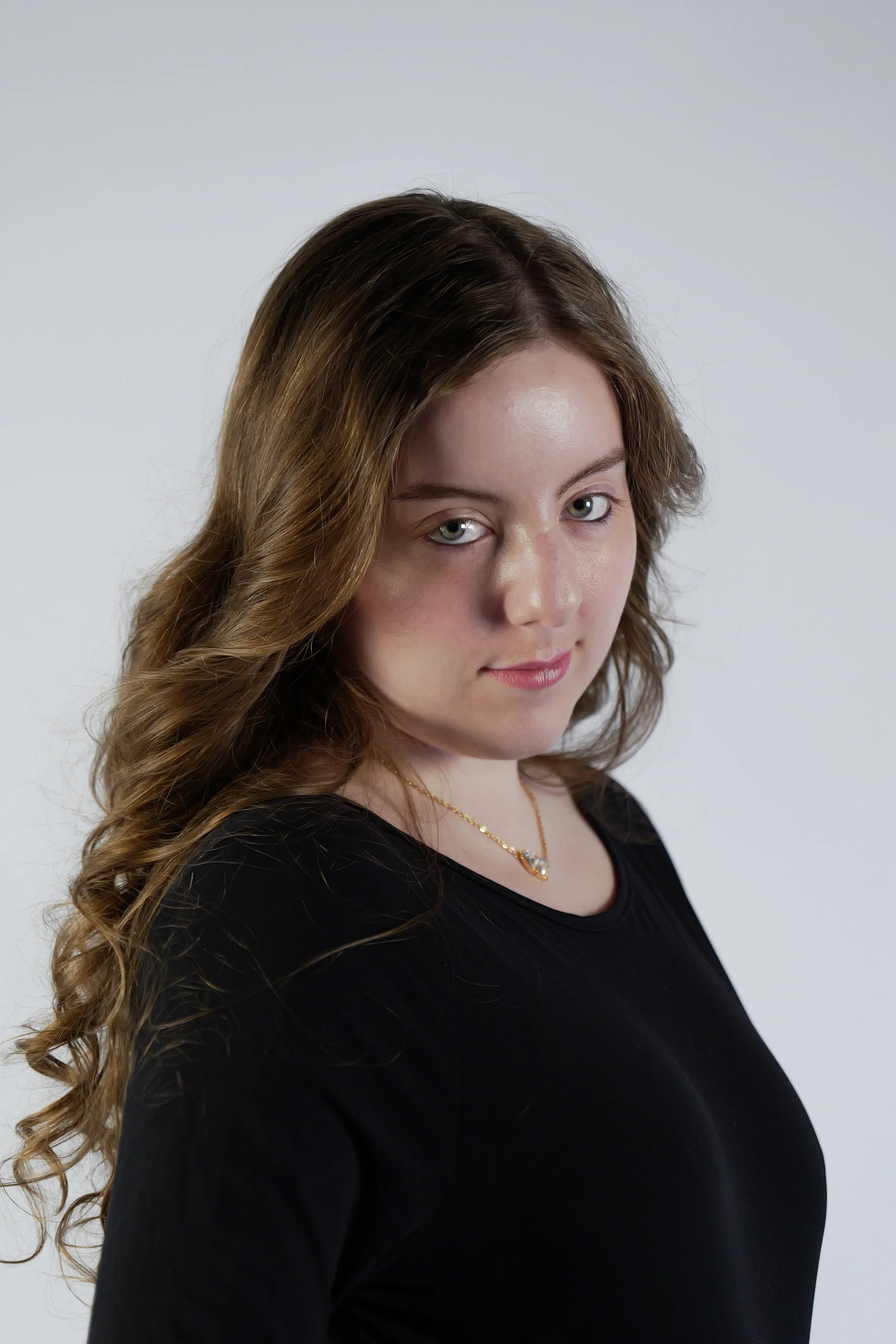 Three-quarter pose with wavy ombré hair, black top, and gold necklace on neutral background