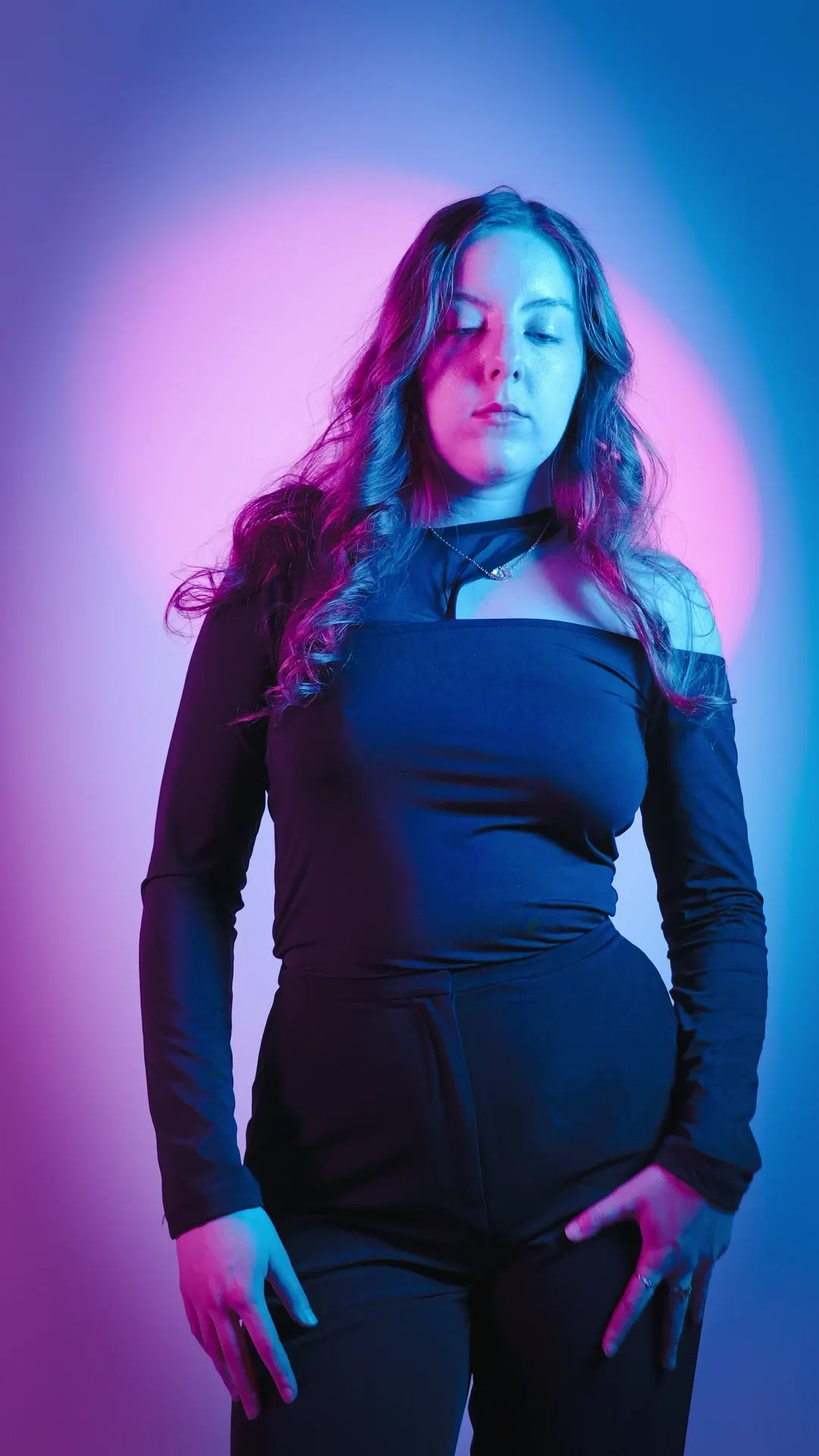 Studio portrait with eyes closed, magenta to cyan gradient lighting, black long-sleeve top