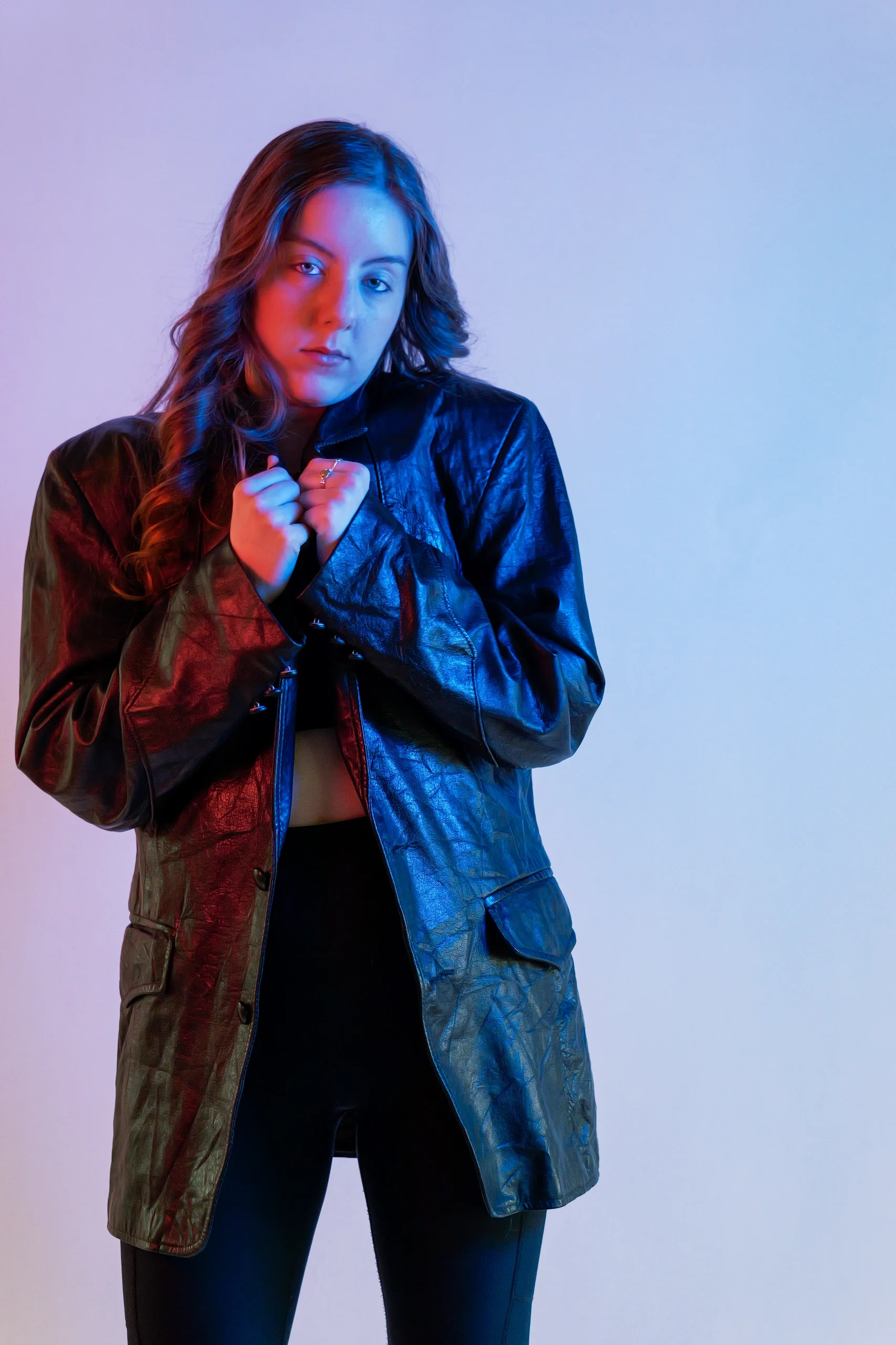 Fashion portrait with red-blue split gel lighting, model in long leather jacket over crop top