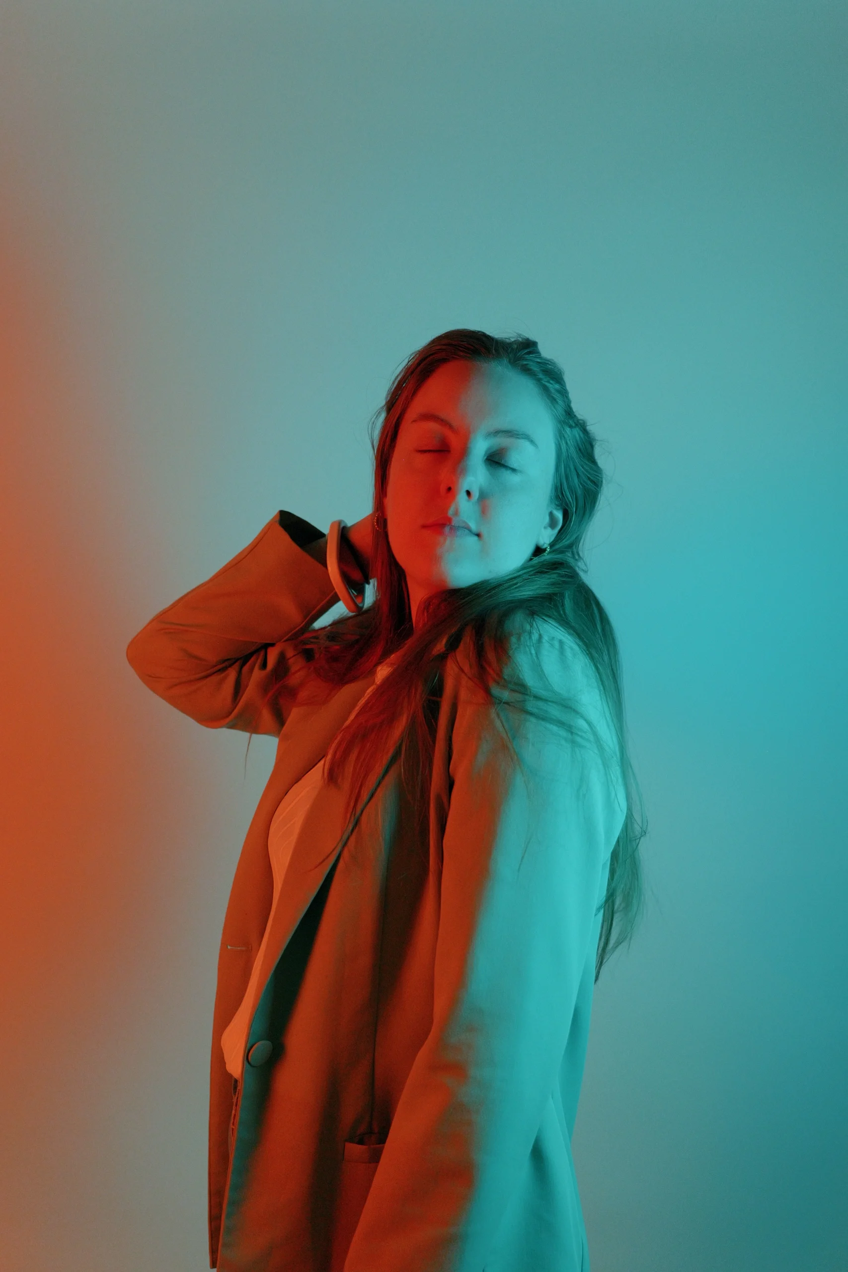 Model in orange jacket, eyes closed, hand in hair, warm orange and cool cyan split gel lighting