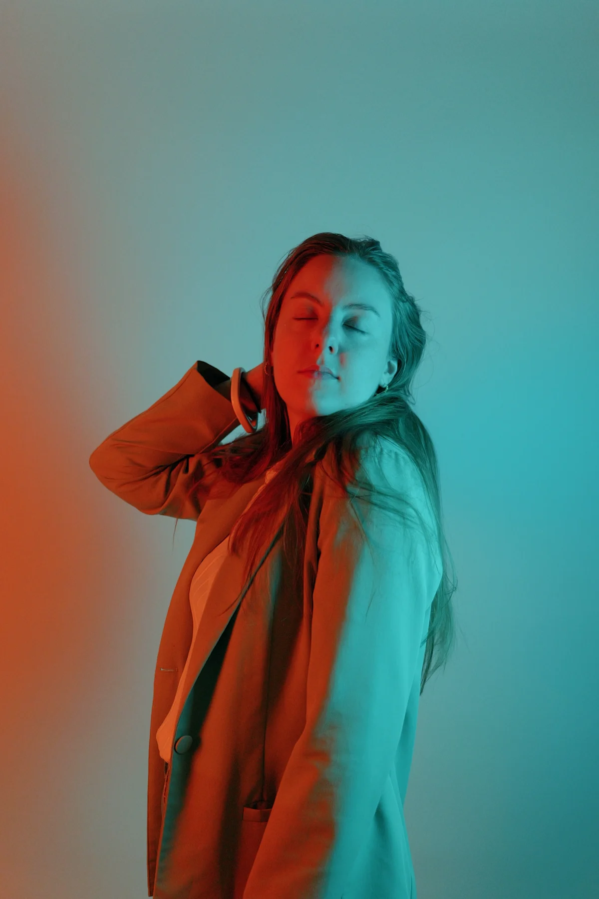 Model in orange jacket, eyes closed, hand in hair, warm orange and cool cyan split gel lighting