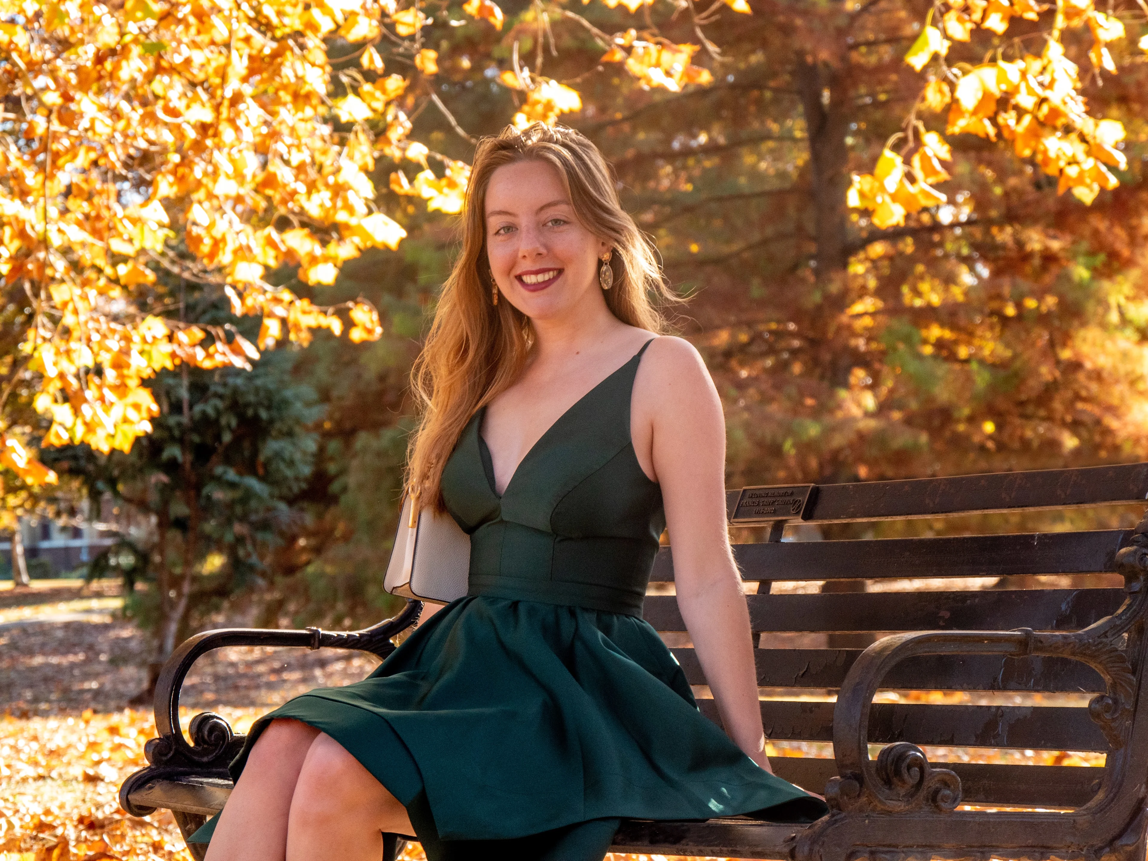 Seated editorial pose in emerald dress with golden hour lighting and autumn leaves backdrop