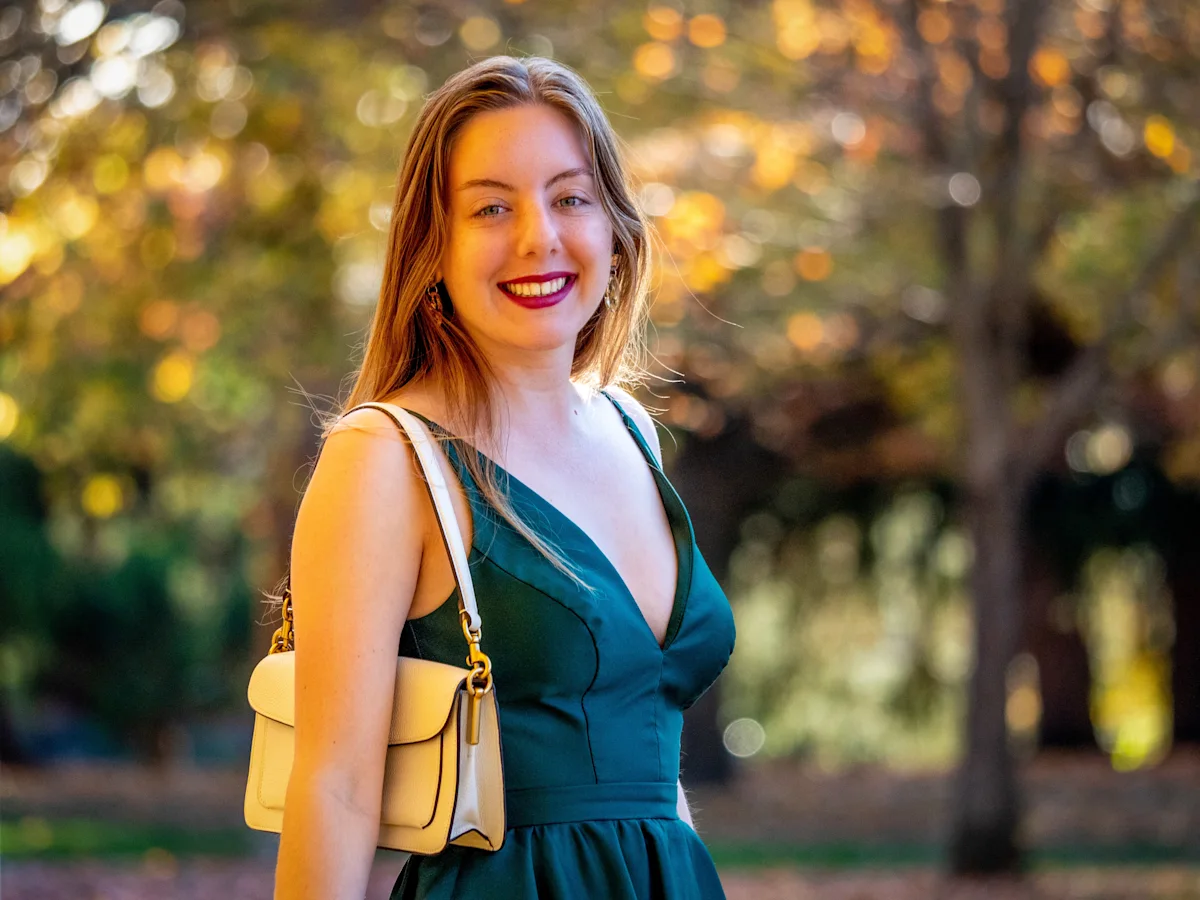 Model in teal dress with yellow shoulder bag, warm golden hour lighting, blurred autumn foliage