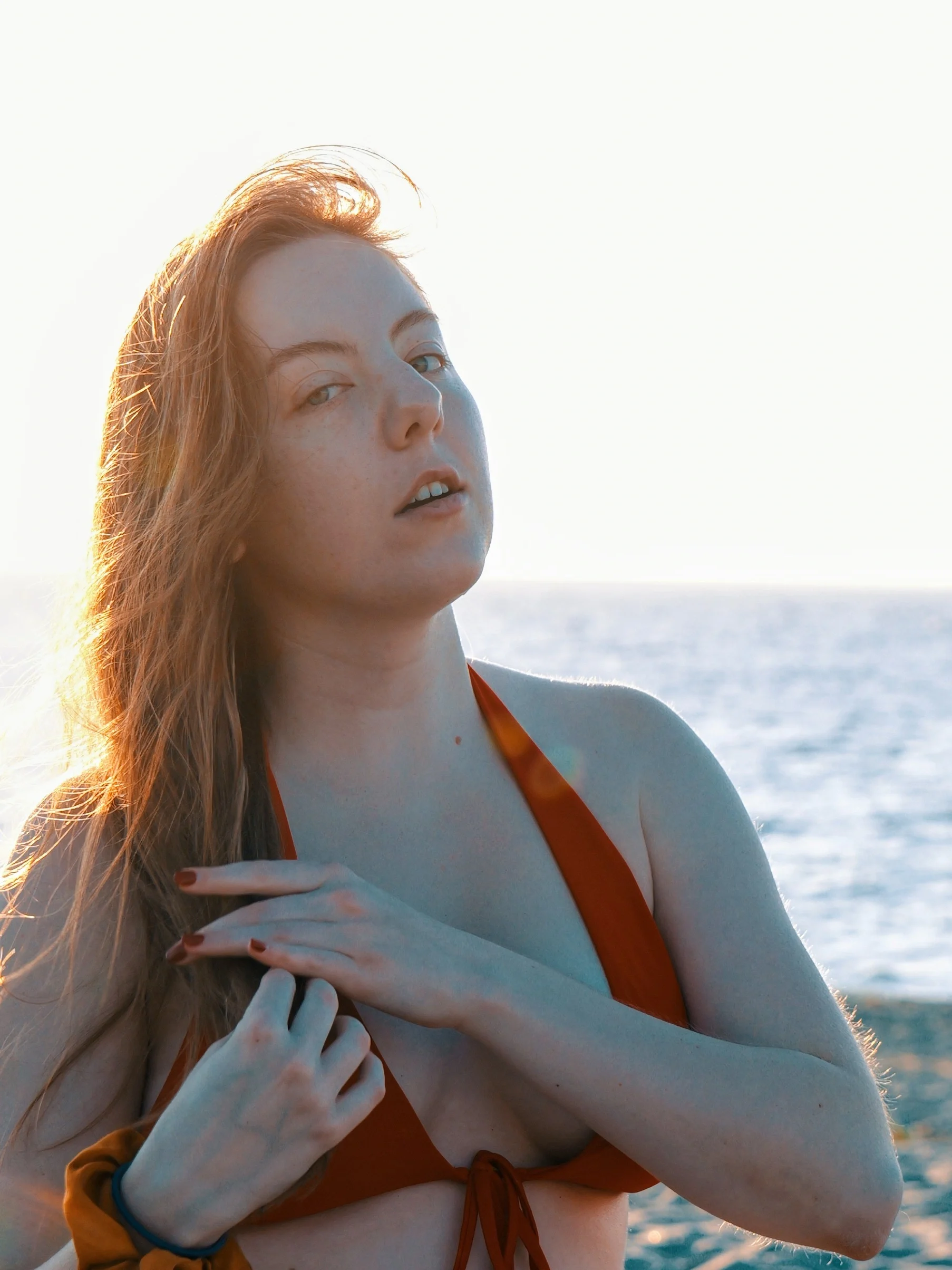 Orange swimsuit, contemplative skyward pose, warm backlighting on hair, ocean background