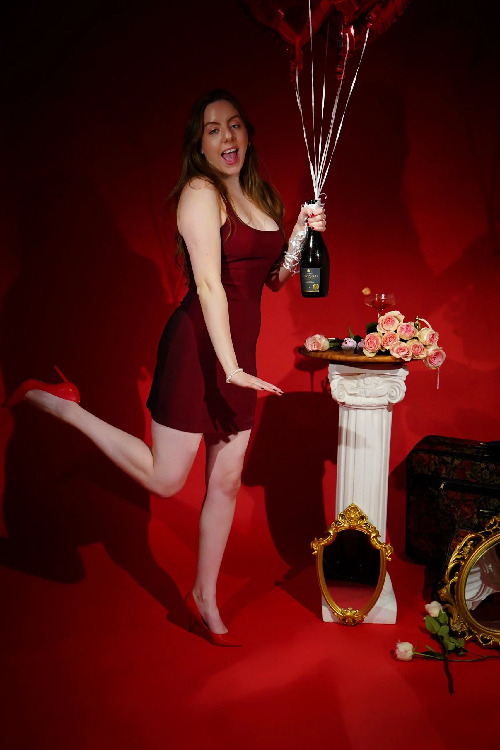 Energetic studio pose in red dress with sparkling champagne against vibrant red backdrop