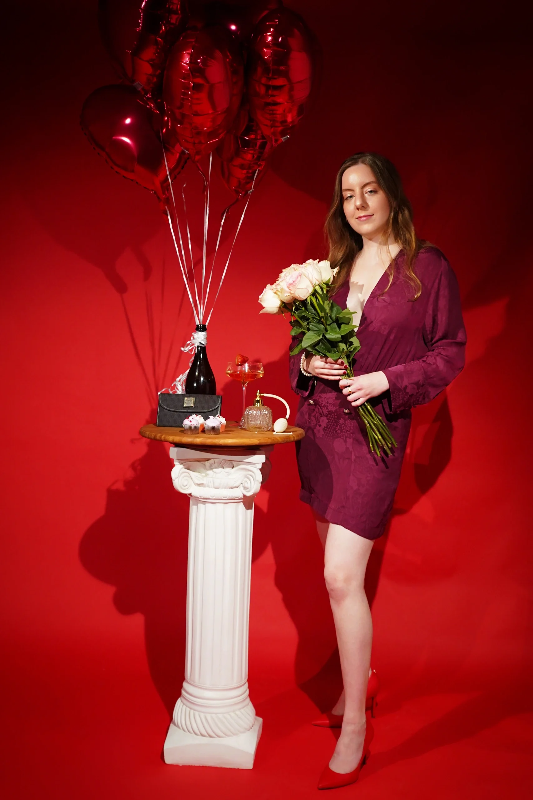 Studio shot in burgundy dress holding white roses with red heart balloons and column styling