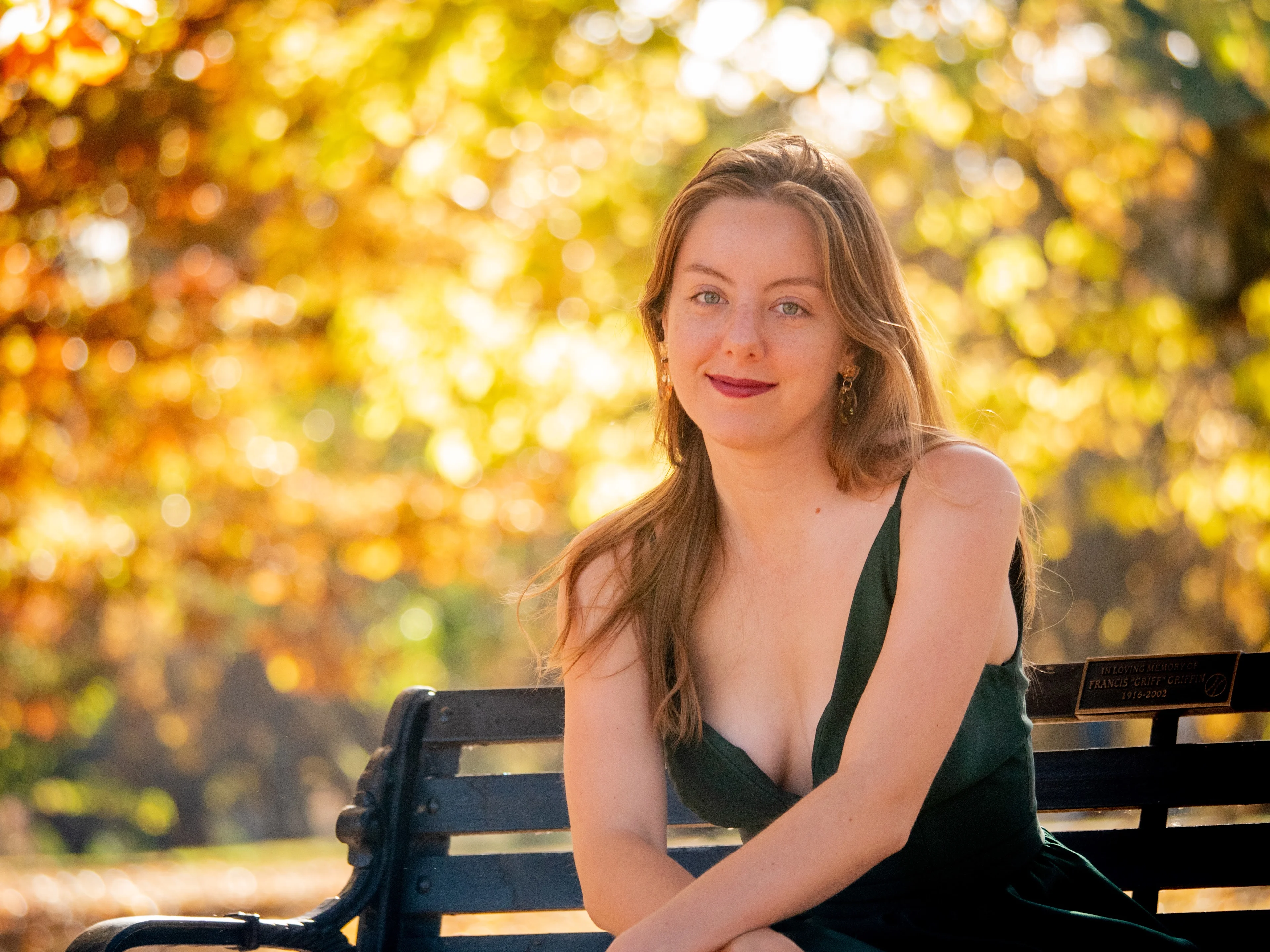 Seated portrait in green dress with golden autumn bokeh and warm afternoon lighting