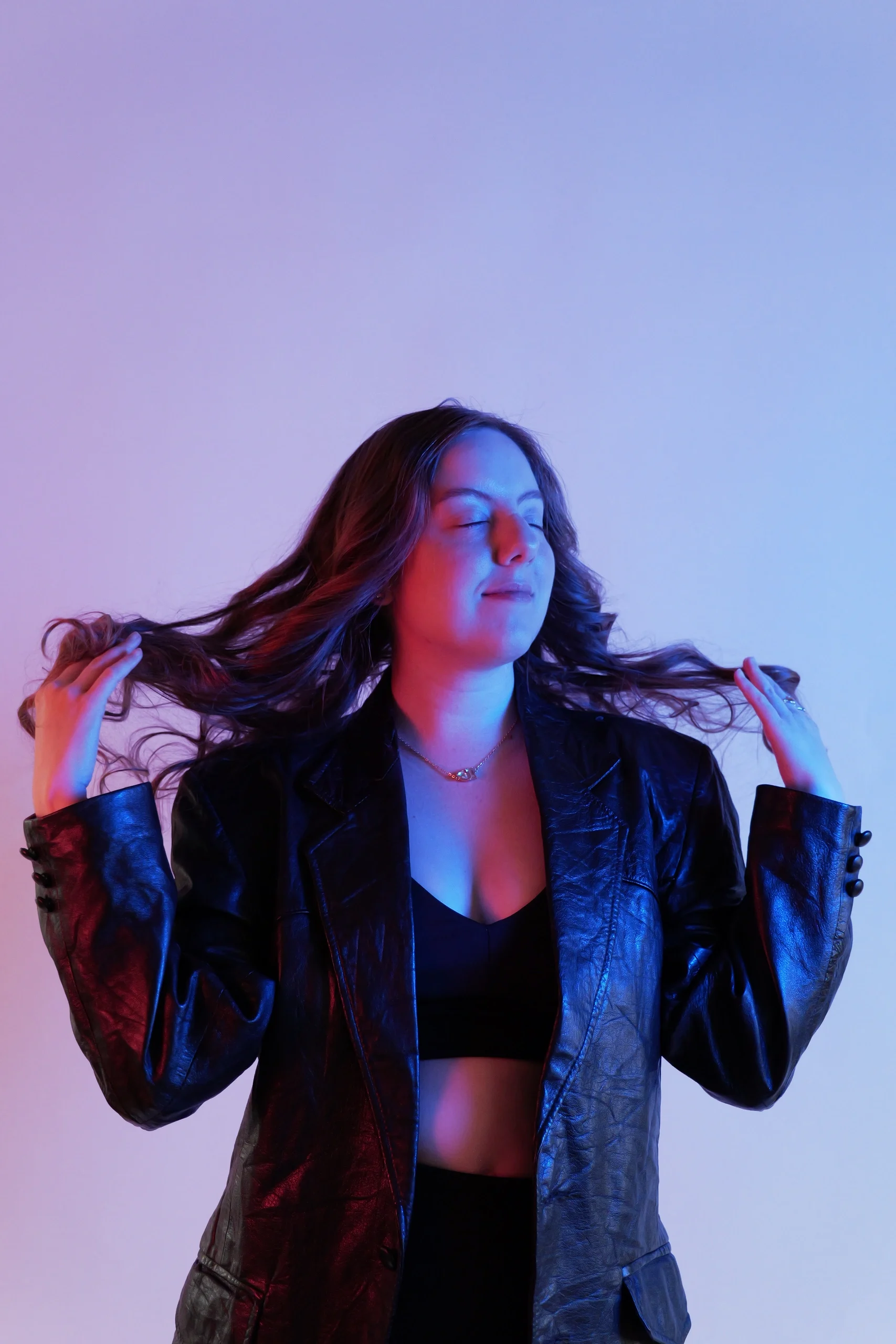 Editorial pose in leather jacket with hands in hair under split red-blue gel lighting