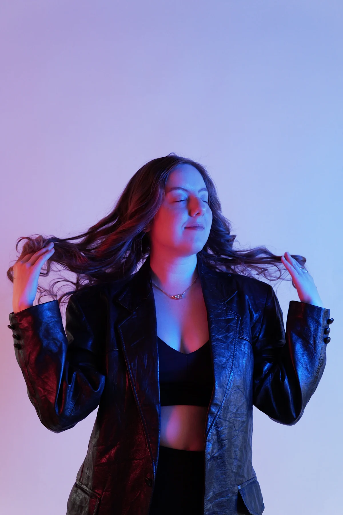 Editorial pose in leather jacket with hands in hair under split red-blue gel lighting