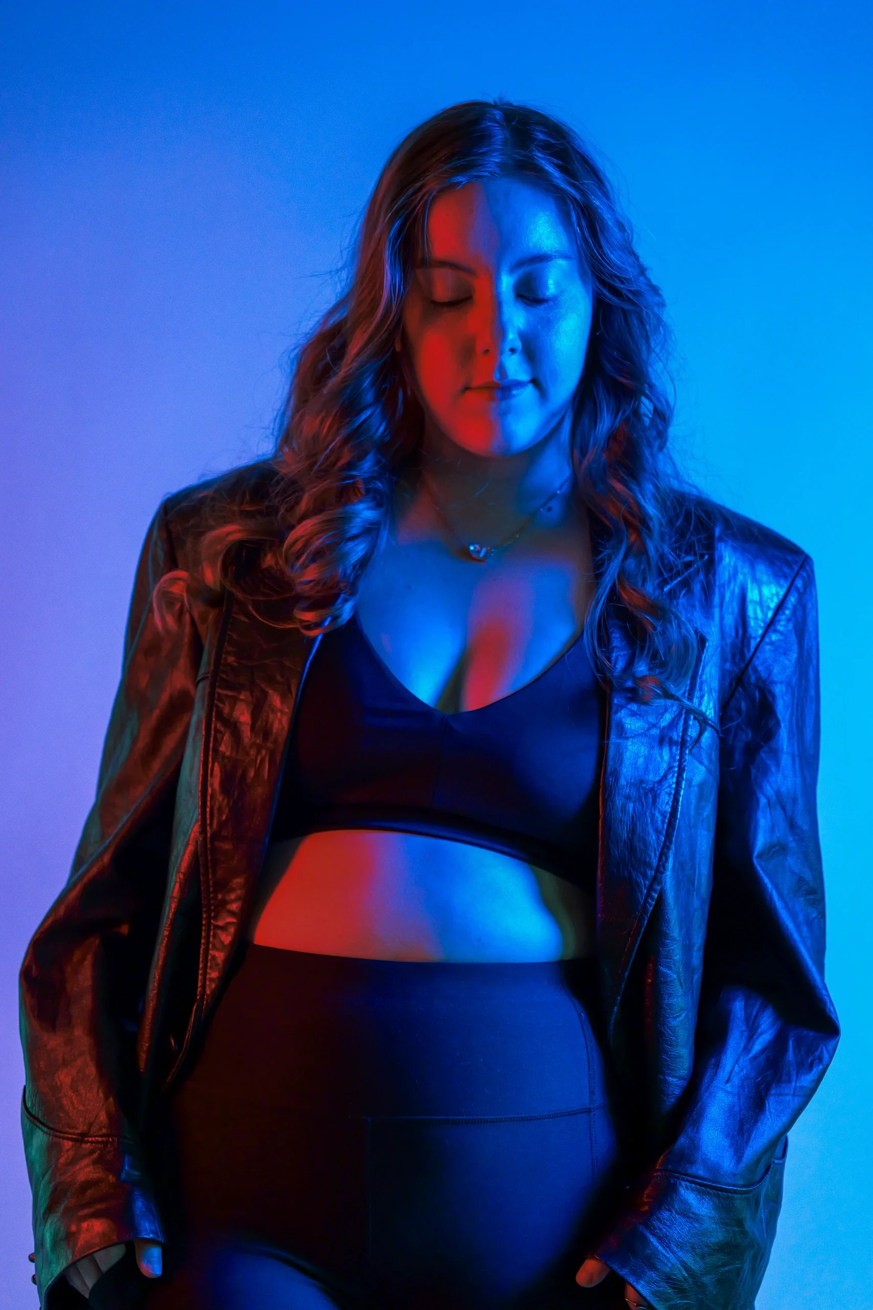 Model in denim jacket with eyes closed, red and blue split gel lighting on blue background