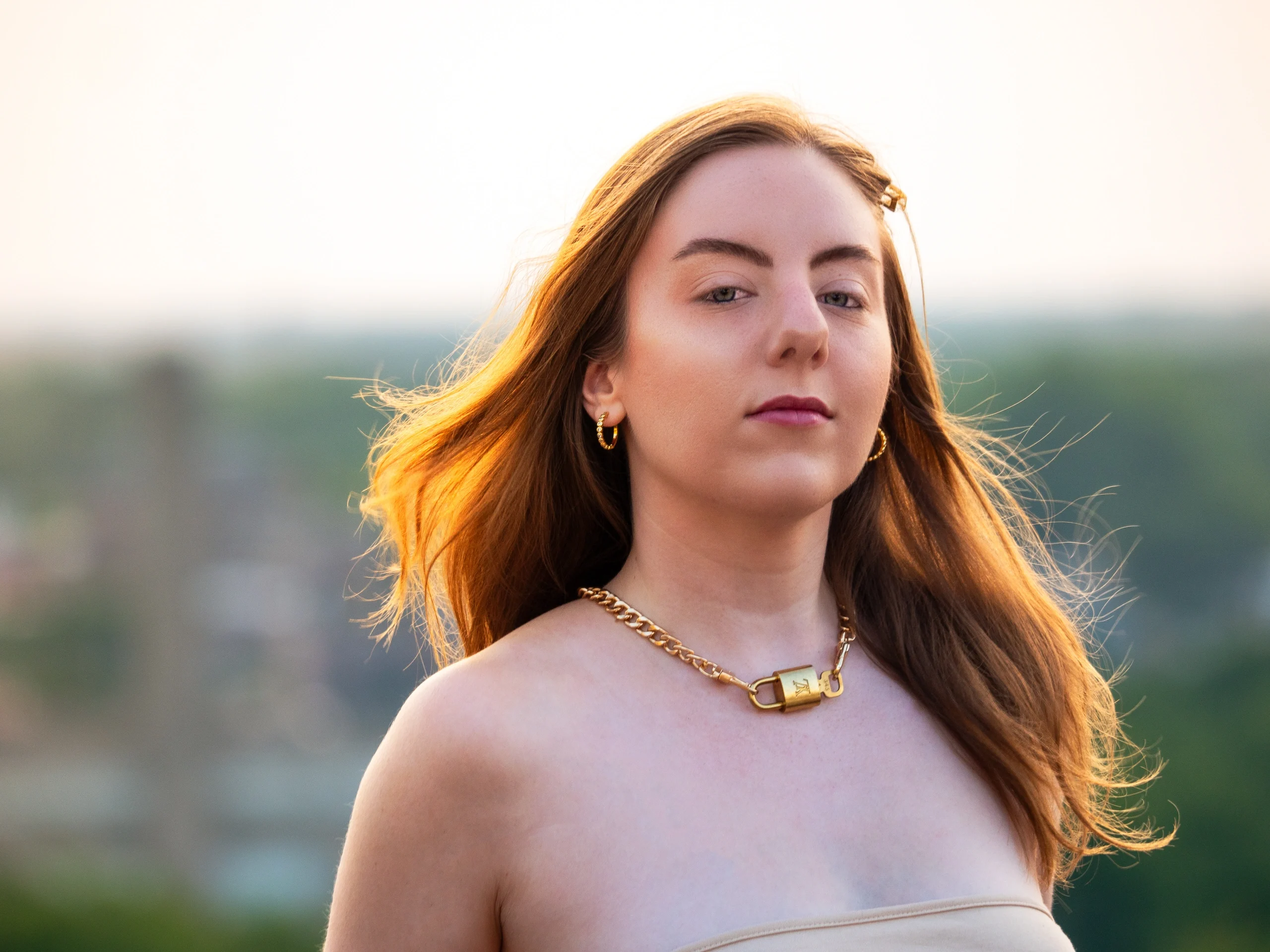 Beige strapless dress, gold chain necklace, hair flowing in wind with warm sunset backlight