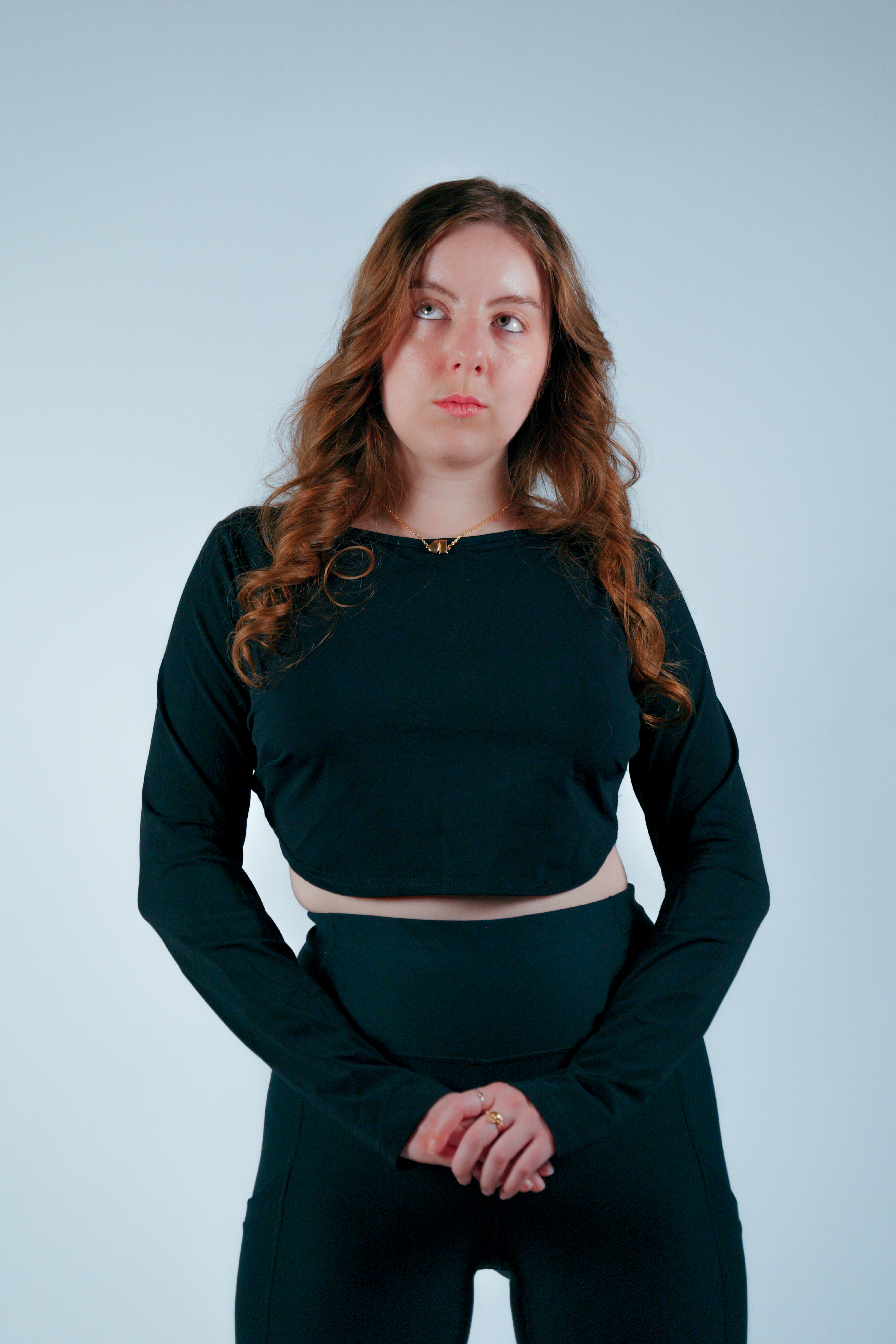 Model in emerald crop top and pants, wavy auburn hair, upward contemplative gaze on pale backdrop