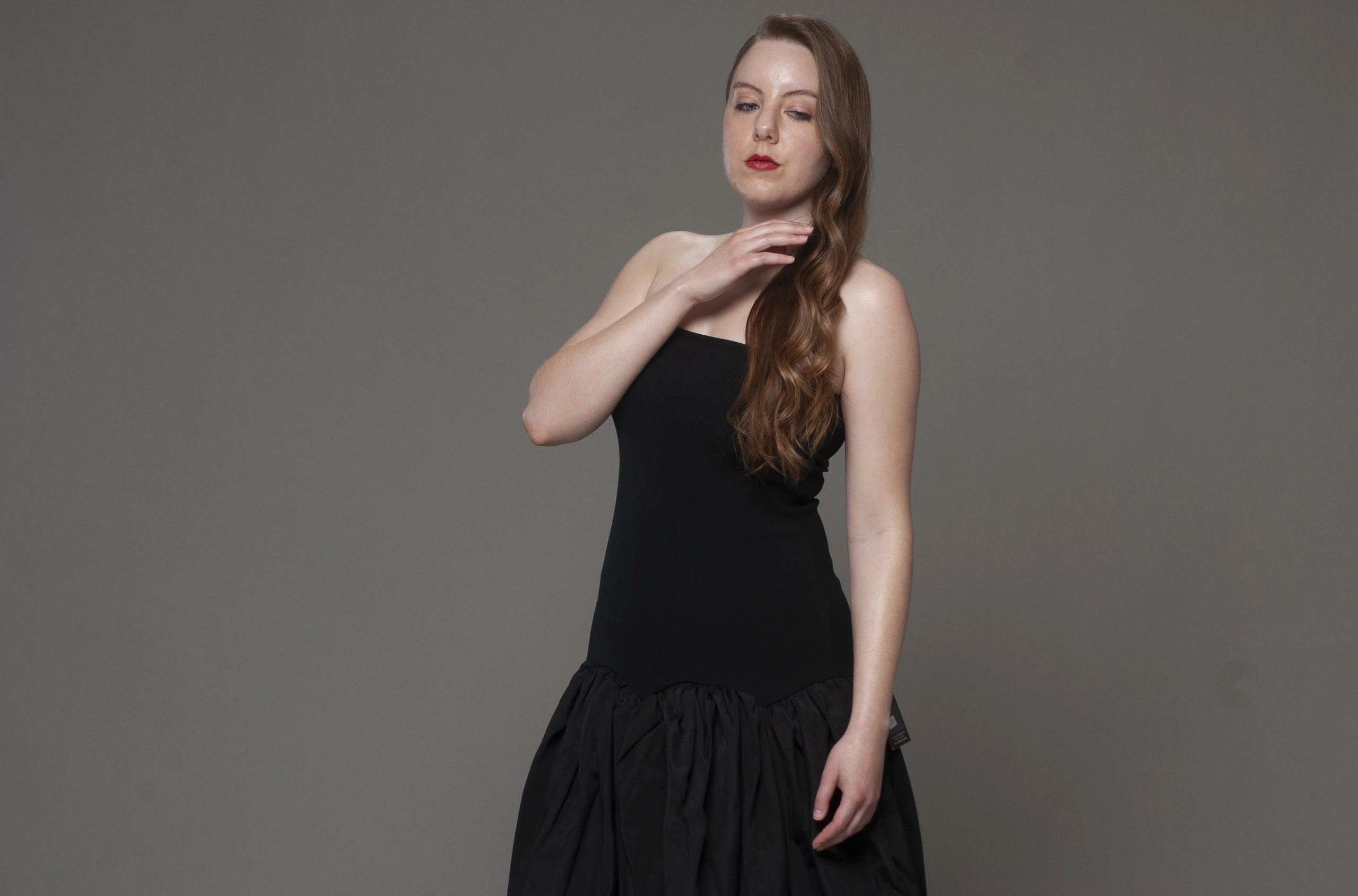 Studio portrait in black drop-waist dress, hand to neck, neutral gray background, soft lighting