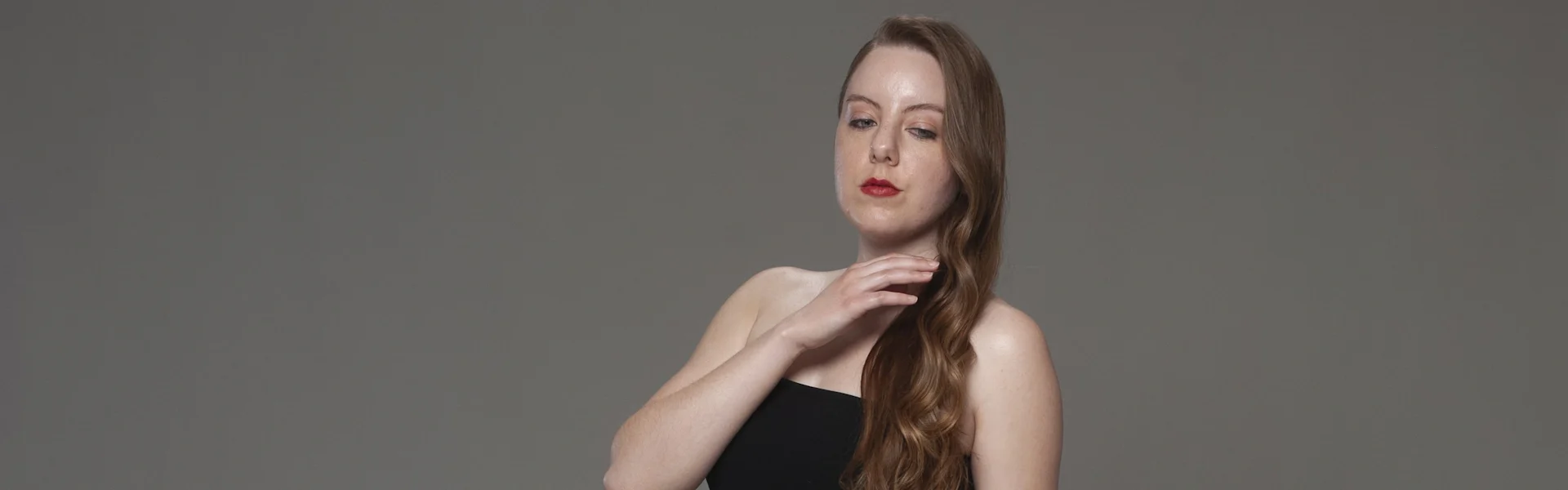 Studio portrait in black drop-waist dress, hand to neck, neutral gray background, soft lighting