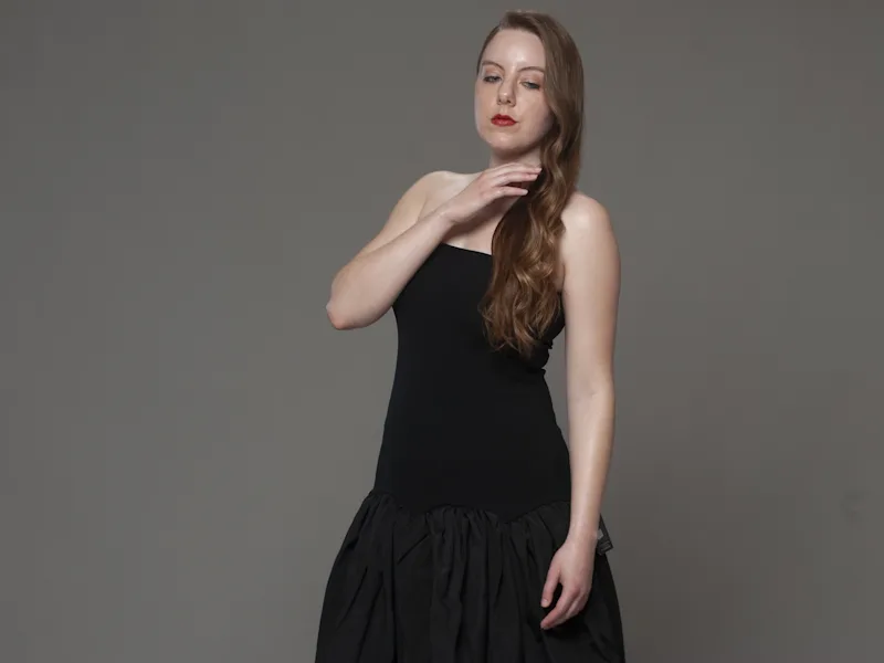 Studio portrait in black drop-waist dress, hand to neck, neutral gray background, soft lighting