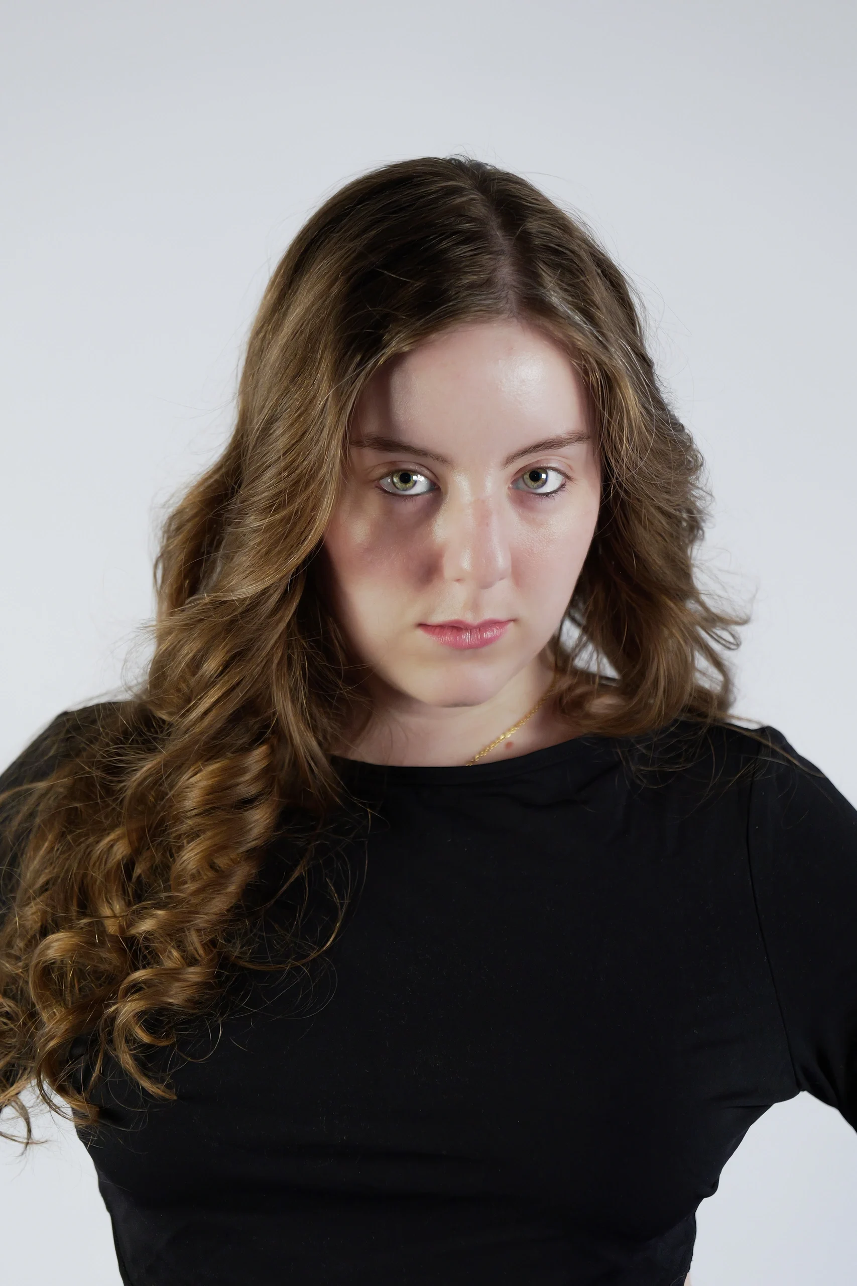 Professional studio portrait in black top, wavy highlighted hair, neutral gray backdrop with even lighting