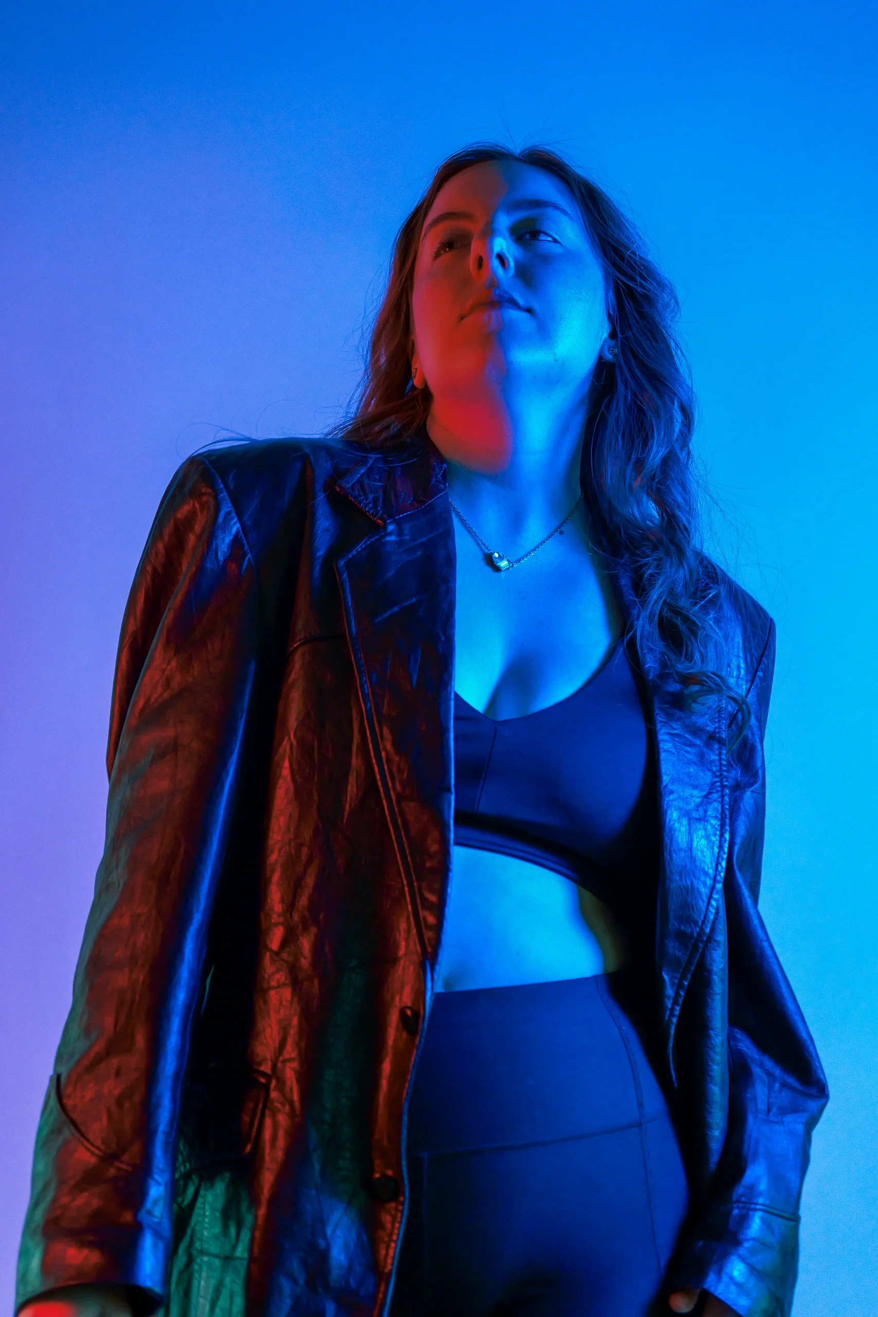 Upward-gazing portrait with dramatic red and blue split lighting and denim jacket