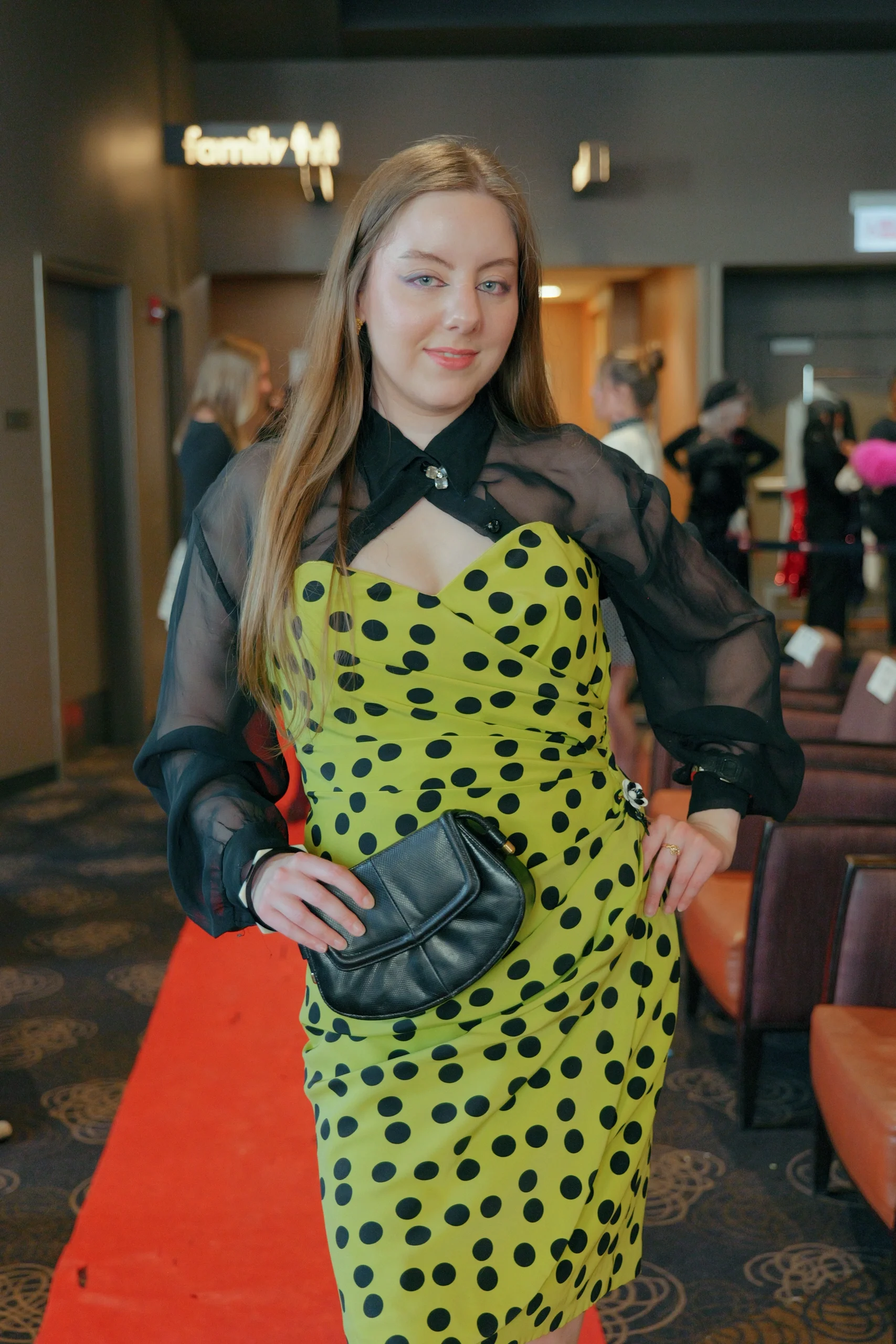 Model in yellow and black polka dot dress with sheer sleeves on red carpet at fashion show