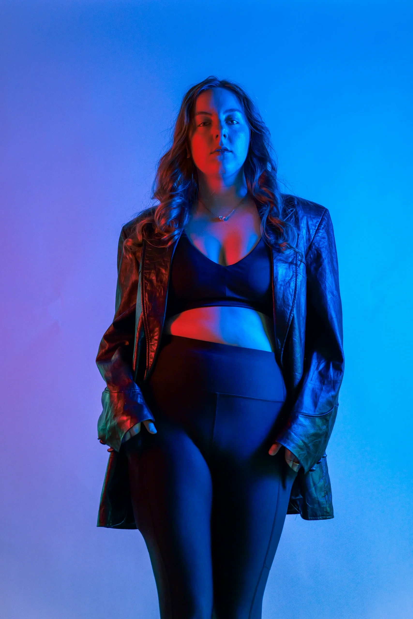 Three-quarter body portrait in denim jacket with red and blue split lighting on blue background