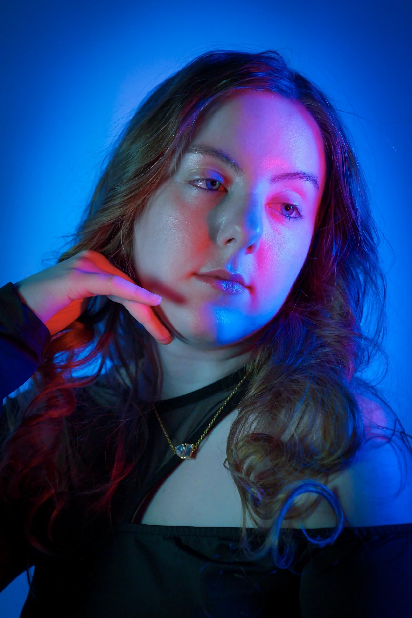 Black leather jacket with gold necklace, hand near face, split magenta and cyan gel lighting