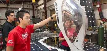 Two students working on a solution model while a third looks on