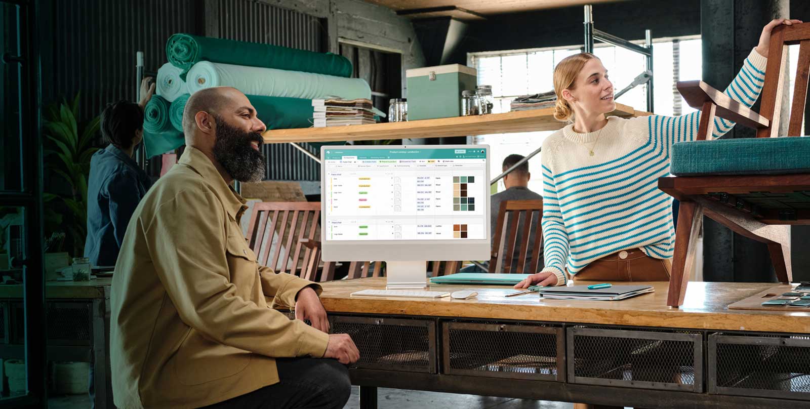 Two workers at a furniture company talk next to a monitor showing their Airtable base