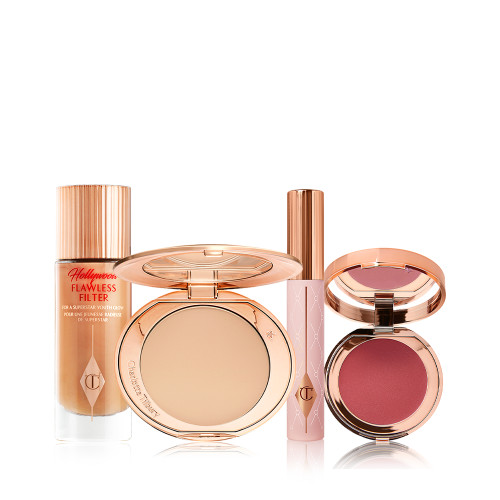 A makeup kit with a glowy primer in a glass bottle with a gold-coloured lid, a pressed powder compact with a mirrored-lid in a soft beige shade, mascara in a nude pink-coloured tube with a gold-coloured lid, and a lip and cheek tint compact with a mirrored-lid in a berry-rose shade.