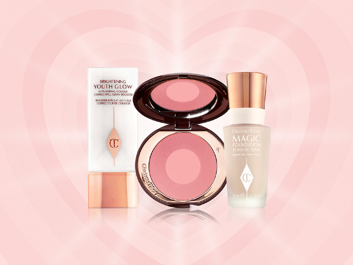 A primer in a white-coloured bottle with gold-coloured lid, an open two-tone blush in muted pink and pearlescent pink, and foundation in a glass bottle with a gold-coloured lid. 