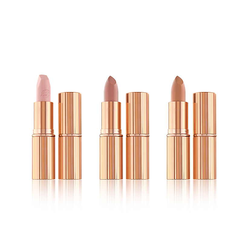 Three, open nude lipsticks in pale, nude colours in golden, metallic packaging. 