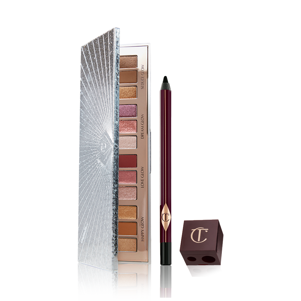 An open eyeshadow palette with twelve eyeshadows in matte and shimmery shades in pink, purple, red, gold, brown, and cream, an eyeliner pencil in black, and a lip and eye pencil sharpener. 