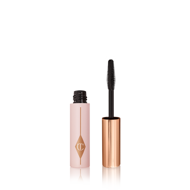 Travel-size mascara in a pink-coloured tube with its gold-coloured applicator next to it. 