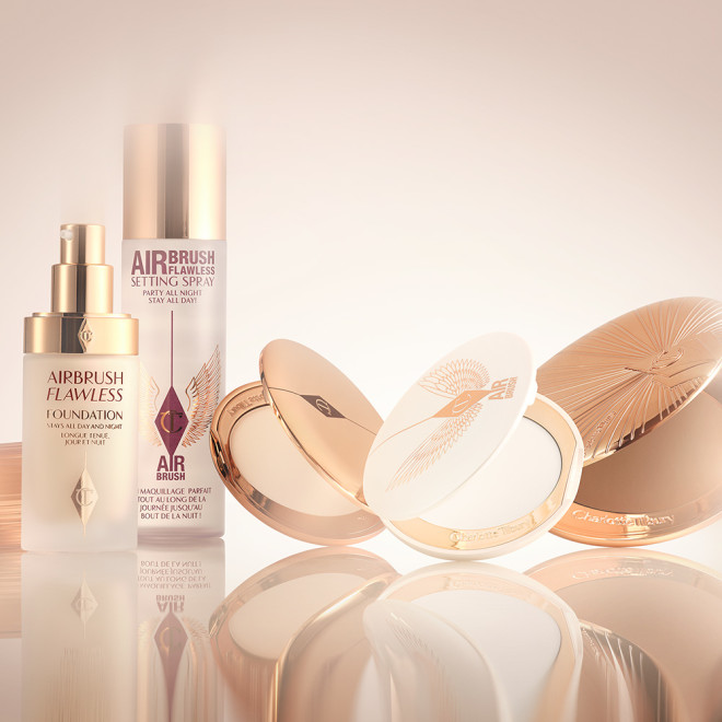 Foundation in a glass bottle with a gold-coloured lid, pressed powder and powder bronzer compacts, cream bronzer compact, and setting spray in a large, clear bottle with a gold-coloured lid.