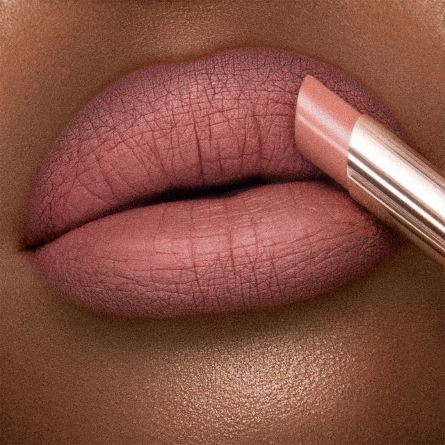 Lips close-up of a deep-tone model wearing a warm peach-nude lipstick with a matte finish.