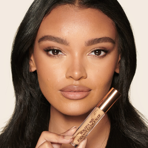 Deep-tone model with brown eyes wearing a radiant, concealer that brightens, covers blemishes, and makes her skin look fresh along with nude lip gloss and subtle eye makeup.