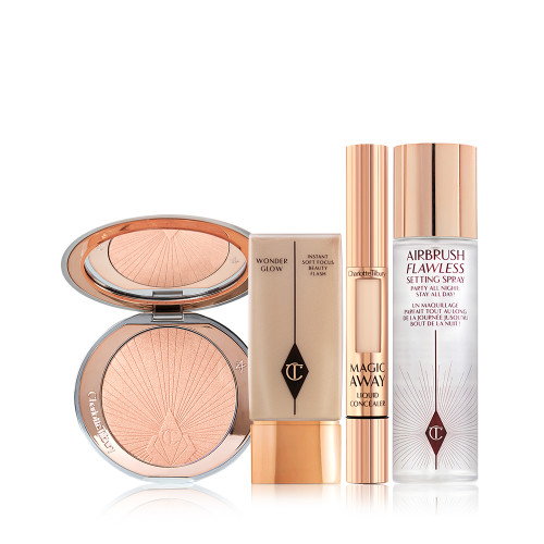 An open, mirrored-lid highlighter compact in a light rose gold shade with a glowy primer in a translucent bottle with a gold-coloured lid, liquid concealer in a gold tube, and setting spray in a clear bottle with a gold-coloured lid.