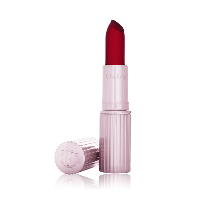 An open glowy, colour-changing lipstick in a sheer red colour with a luminous purple-coloured tube and lid. 