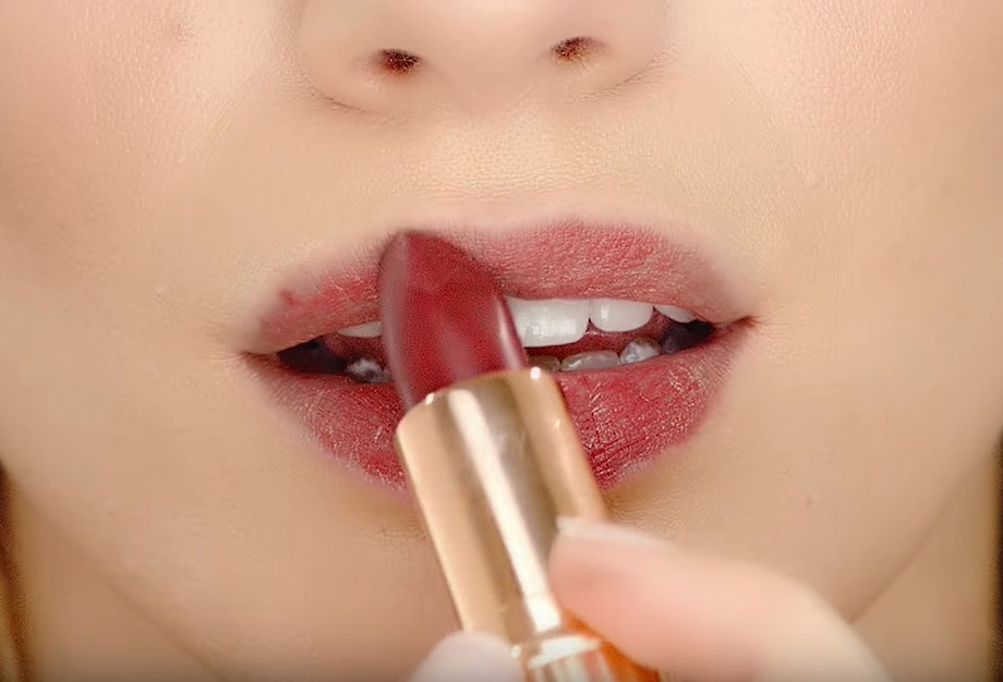 Close-up of a light-tone model applying a berry-rose matte lipstick. 