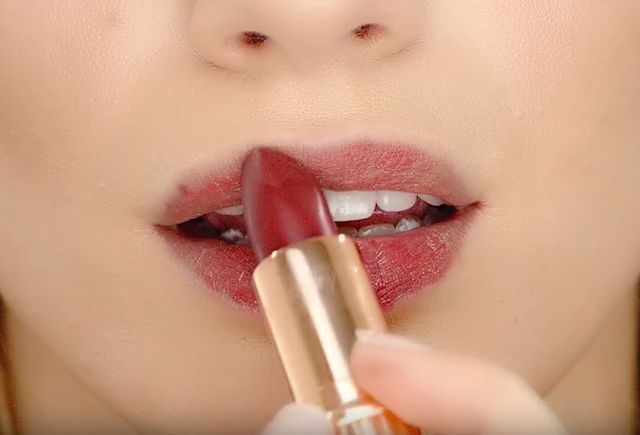 Close-up of a light-tone model applying a berry-rose matte lipstick. 