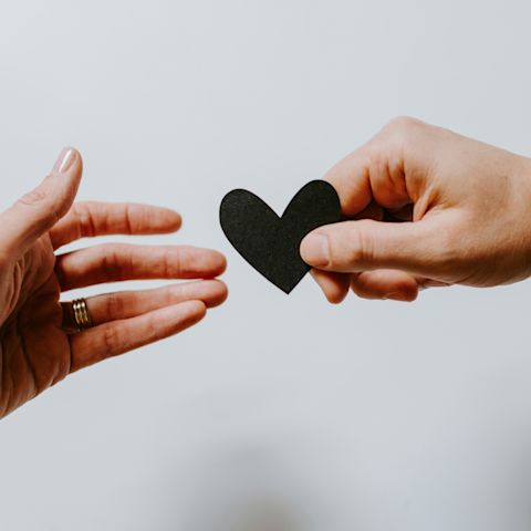 One hand giving a paper heart to another hand as an act of kindness 