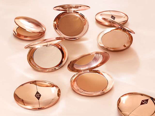 A collection of pressed powder compacts for light, medium-light, fair, and deep tones, in gold-coloured packaging with mirrored lids.