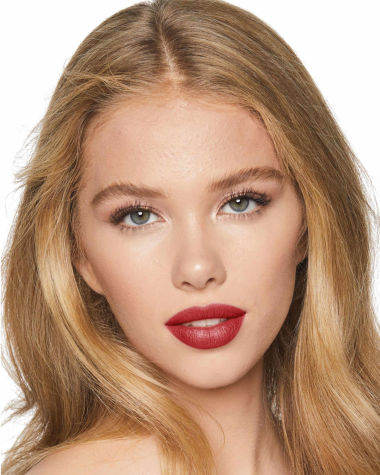 A fair-tone brunette model with grey eyes wearing shimmery beige and cream-coloured eyeshadow with a vibrant, poppy-red lip tint. 