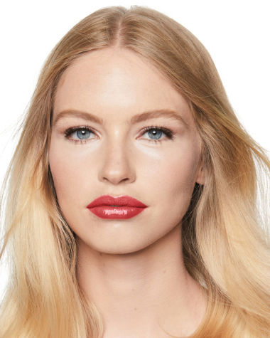 Fair-tone model with blue eyes wearing a moisturising lipstick balm in a peach rose shade with a high-shine finish.