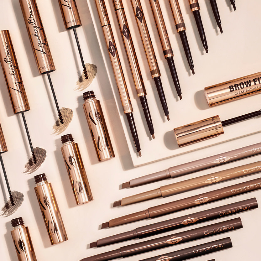 A collection of open eyebrow tints, eyebrow pencils, and eyebrow gels in gold-coloured packaging,