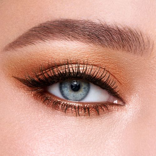 Single-eye close-up of a fair-tone model with blue eyes wearing shimmery peach and smokey copper eyeshadow with black eyeliner.