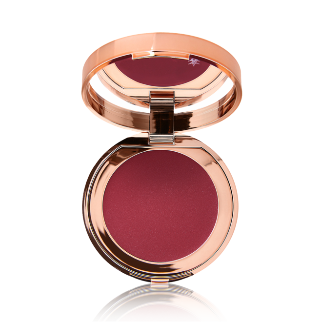 An open, mirrored-lid lip and cheek cream compact in a berry-red shade. 